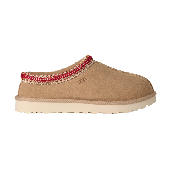 The UGG Women's Tasman II Sand slipper features tan suede, a textured sole, light beige lining, and red and white stitching along the top edge. The UGG logo appears on the side.