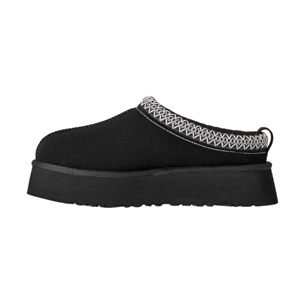The UGG Women's Tazz II Black is a black slip-on mule by UGG, featuring a thick sole, white zigzag stitching on the upper edge, and soft sheepskin lining for comfort, displayed against a white background.