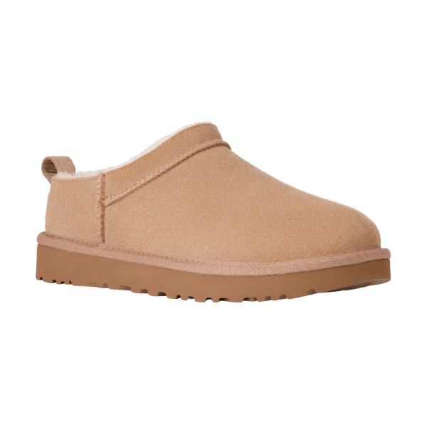 The UGG Women's Classic Micro Sand slipper features tan suede, a low back, rounded toe, heel pull tab, thick rubber sole, and a soft lining for warmth and comfort. Inspired by the classic UGG design.