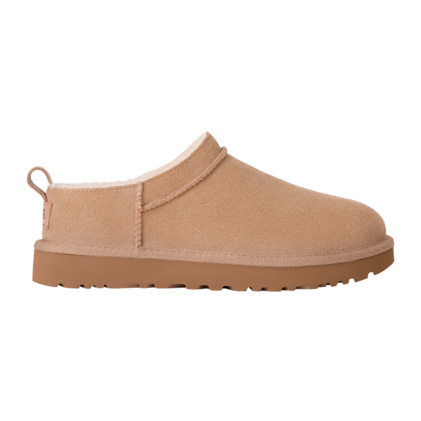 The UGG Women's Classic Micro Sand slipper by UGG is a tan suede slip-on with a thick rubber sole and white fleece lining, inspired by sheepskin boots and shown from the side on a white background.