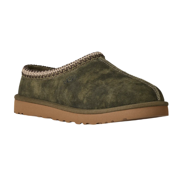 The UGG Men's Tasman Baxter in Burnt Olive features a green suede slip-on upper, tan stitching at the opening, brown rubber sole, subtle UGG branding on the side, and cozy UGGplush lining for comfort.