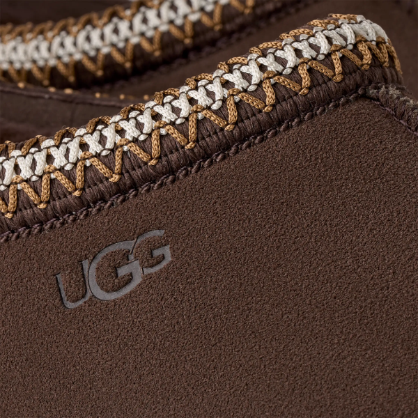 Close-up of the UGG Men's Tasman II Cocoa shoe, showcasing white and tan stitching, a soft suede upper with an embossed UGG logo, and plush sheepskin lining for comfort.