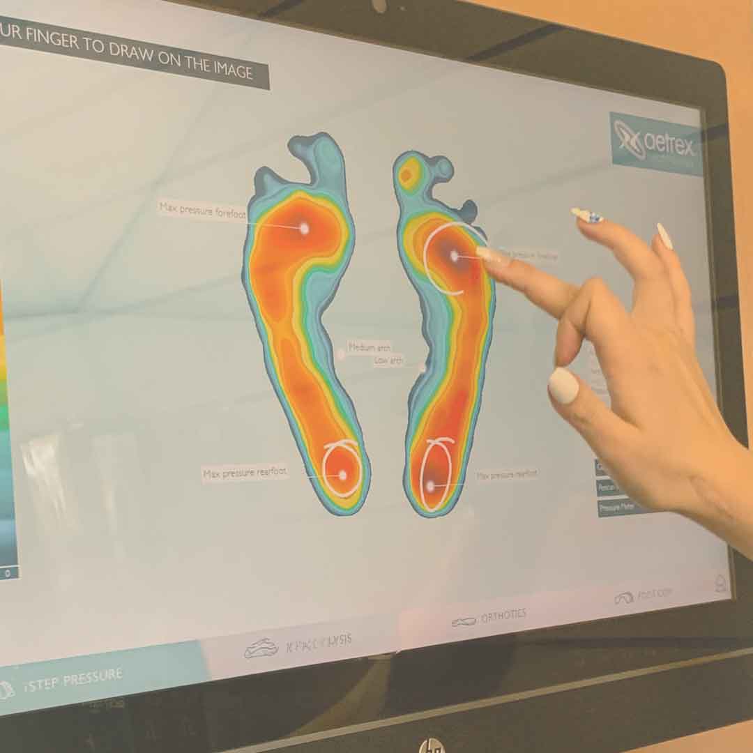 A person points at a computer screen showing the Book Your Appointment feature by Lucky Feet Shoes, displaying a colorful foot pressure map with areas of varying pressure on both feet.