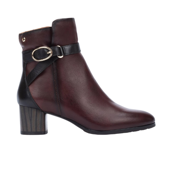 The PIKOLINOS Women’s Calafat Dark Brown ankle boot features dark brown leather, a medium block heel, black accents, and a decorative black strap with a gold buckle around the ankle.