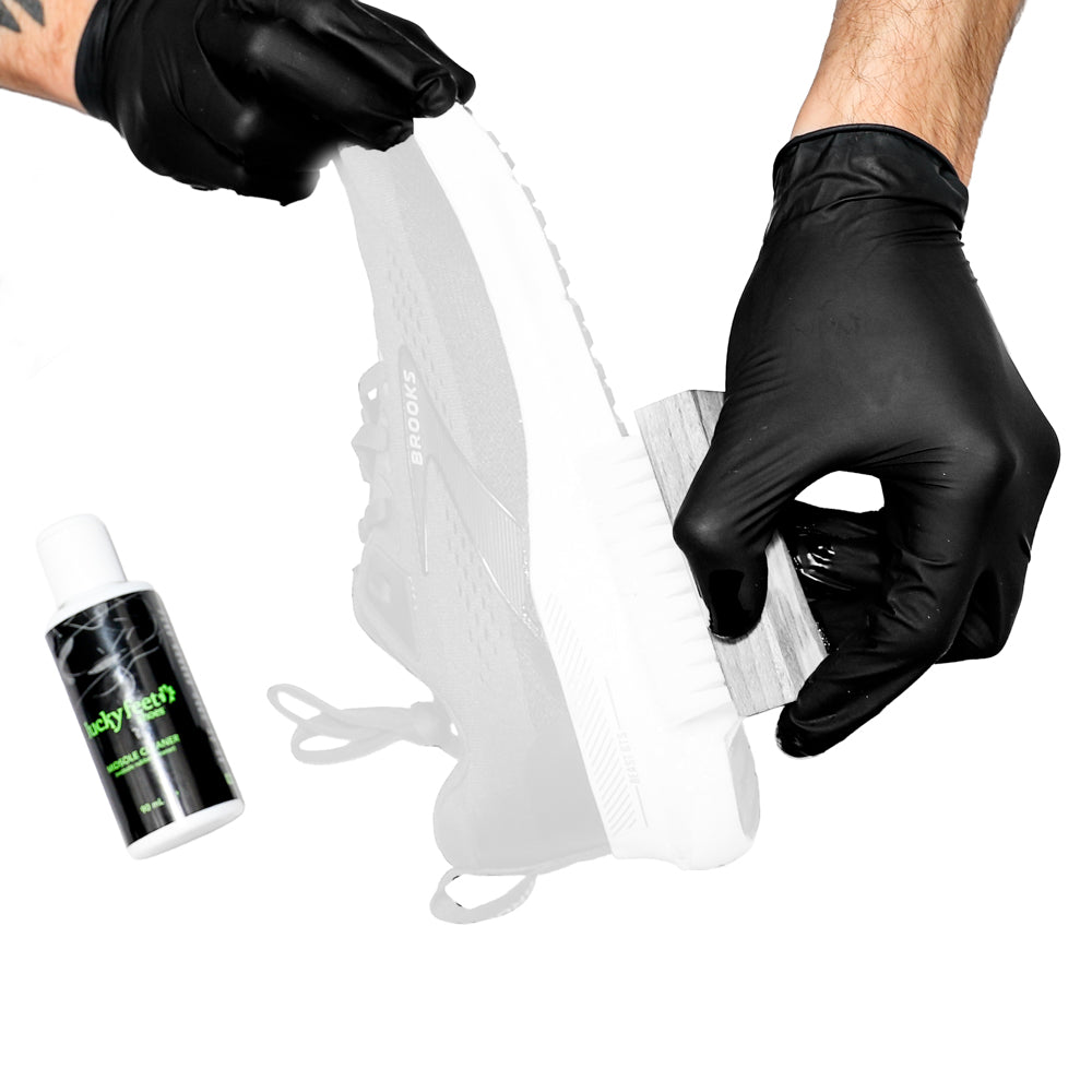 Person cleaning a white shoe with black gloves, using a spray bottle and cloth, on a white background.