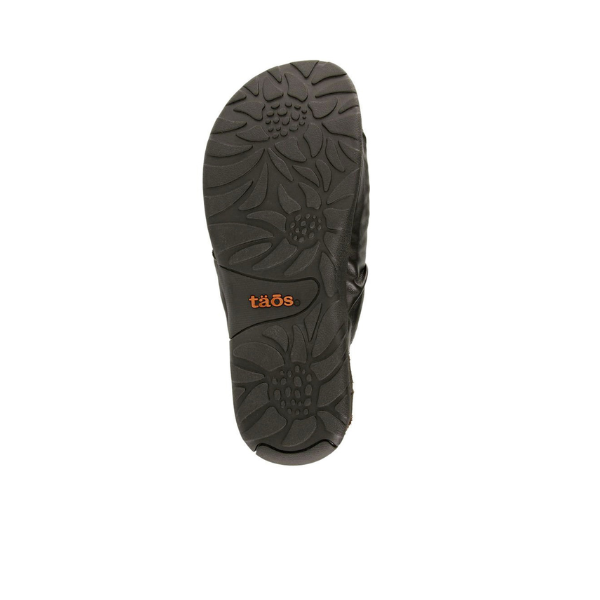 The sole of the TAOS Womens Gift 2 Sandal Black features a floral-patterned tread and an orange taös logo, designed for arch support and foot pain relief. The sandal is pictured on a white background.