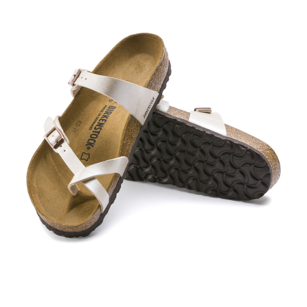 A pair of BIRKENSTOCK Womens Mayari Birko-Flor Graceful White Pearl sandals with contoured cork footbeds and white straps. One sandal stands upright, the other lies sideways, revealing the textured black sole.