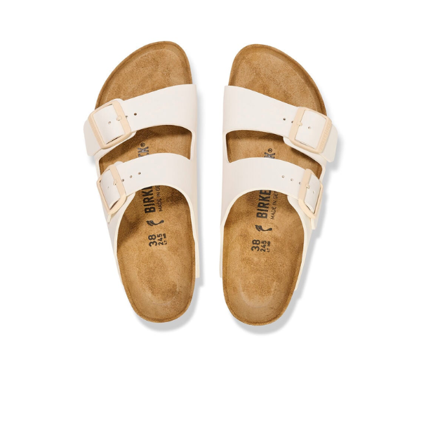 The BIRKENSTOCK Womens Arizona Birko-Flor Patent Offwhite/Eggshell sandals feature cork footbeds and adjustable buckles, offering stylish everyday comfort. Shown from above on a white background.