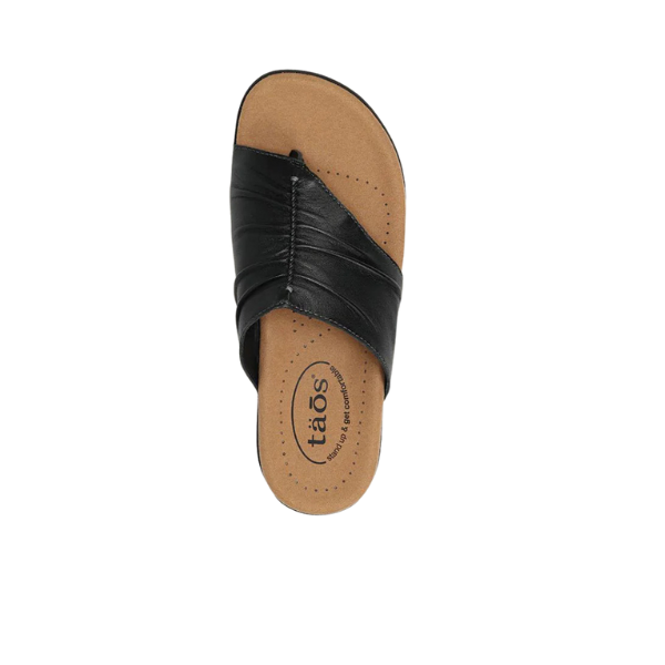 A single TAOS Womens Gift 2 Sandal in black, featuring a tan cushioned footbed and arch support with the TAOS logo on the insole, is seen from above against a white background.