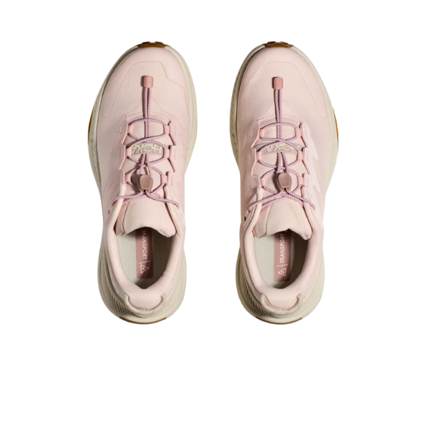The HOKA Womens Transport in Cosmic Pearl/Oat Milk/Pink are vegan athletic sneakers with mauve laces and white soles, designed by HOKA to help reduce foot pain, shown from above against a white background.