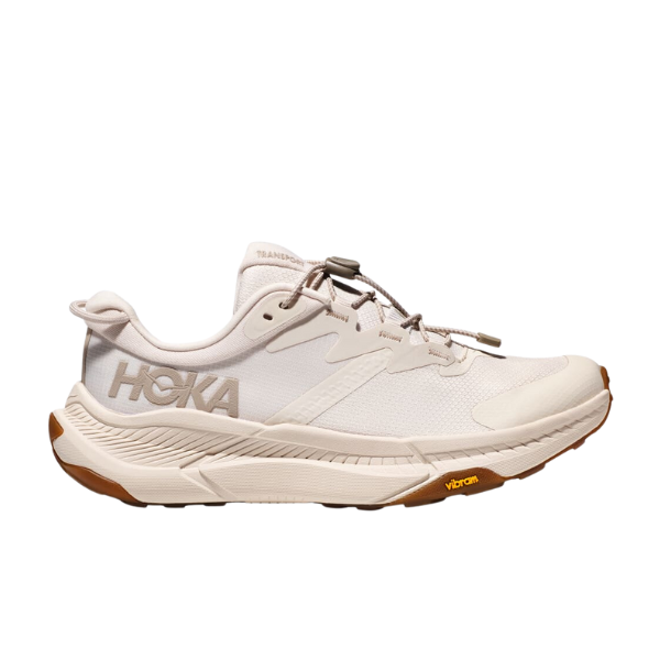 A side view of the HOKA Womens Transport Wide Neutral sneaker in white with beige accents, featuring a chunky VIBRAM outsole, lace-up closure, and crafted with vegan materials.