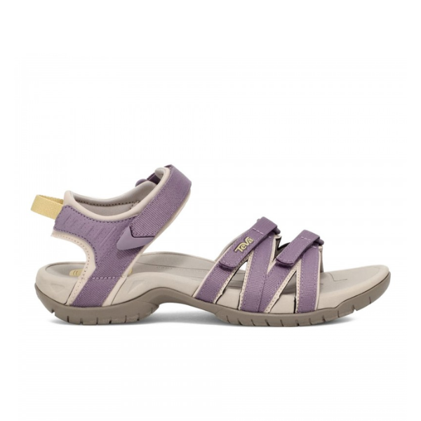 The Teva Women’s Tirra Grey Ridge/Purple sport sandal features adjustable purple straps, Velcro ankle closure, a rugged beige sole, yellow logo tag, and pull tab—offering comfort and support in a stylish design.