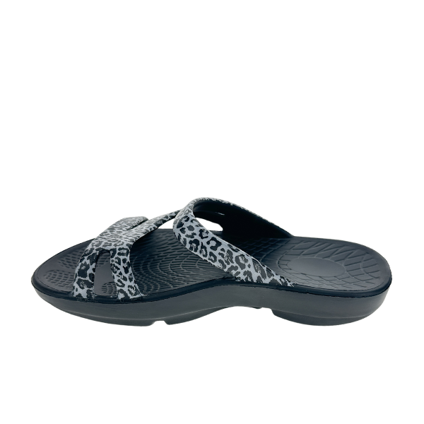 The Sovella Womens PF Slide Black/Leopard by SOVELLA features black crisscross straps in a gray and black leopard print, a textured sole, and delivers exceptional arch support and comfort recovery, shown on a white background.