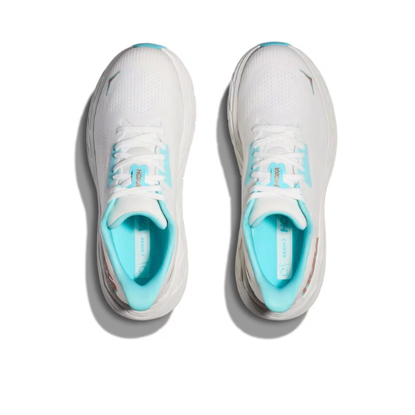 A pair of HOKA Womens Arahi 7 (Medium Width) White/Gold running shoes from HOKA, shown from above with a light blue inner lining and laces, featuring J-Frame™ technology for support on a plain white background.
