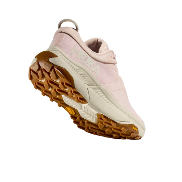 The HOKA Womens Transport in Cosmic Pearl/Oat Milk/Pink features a light pink upper, thick white midsole, and textured tan outsole—designed to reduce foot pain—displayed at an angle to show the sole and HOKA logo on a white background.