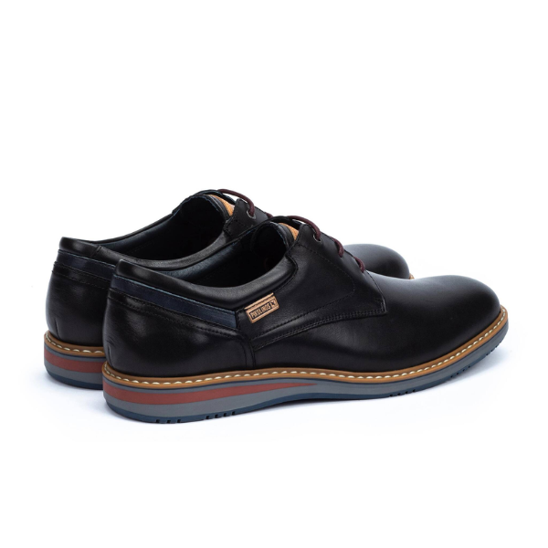 The PIKOLINOS Mens Avila Black dress shoes feature black leather, blue and brown rubber soles, decorative stitching, and a metallic side label. Designed for foot pain comfort, theyre shown on a white background.