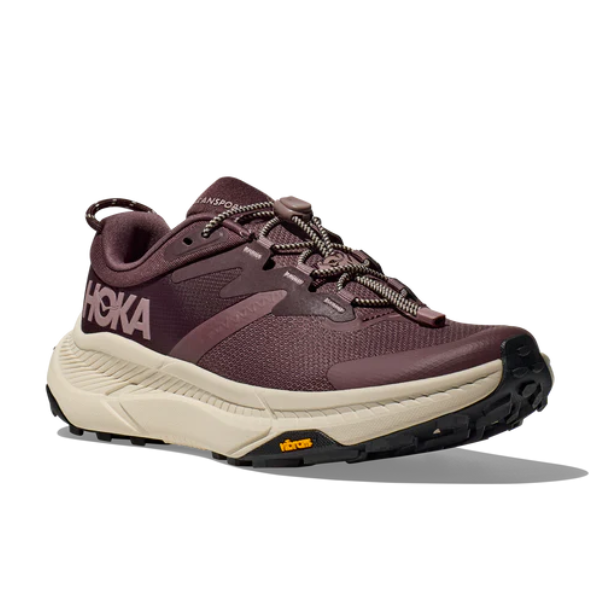 The HOKA Womens Transport in Smoky Quartz/Oat Milk/Purple features a maroon upper, beige sole, Vibram outsole with black tread, and a white HOKA logo on the side, displayed at an angle on a white background.