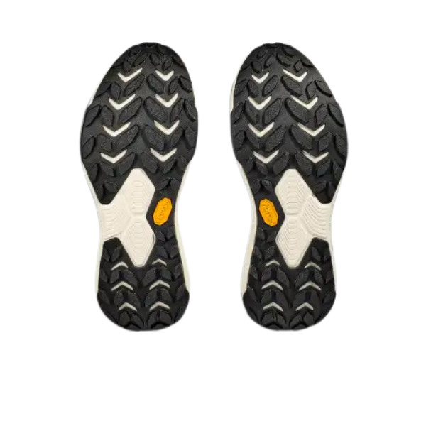 A pair of HOKA Womens Transport (Wide Width) Black/White shoe soles with a rugged zigzag tread and yellow VIBRAM® logo, crafted from vegan materials, shown against a white background.