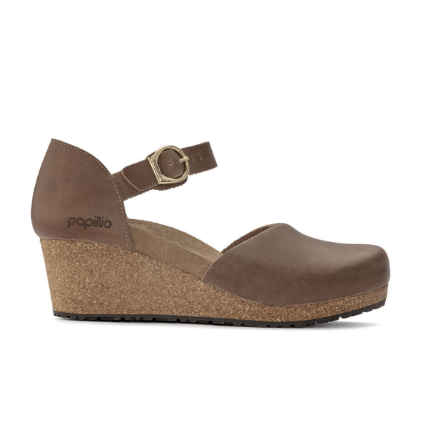 The Birkenstock Womens Mary Leather Cognac wedge shoe features a closed toe, cork sole, ankle strap with gold buckle, and a side heel displaying the Papillio logo by BIRKENSTOCK.
