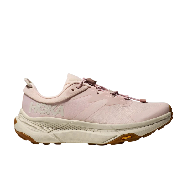 The HOKA Womens Transport in Cosmic Pearl/Oat Milk/Pink is a vegan running shoe with a white and tan sole, Vibram logo by the toe, and bold HOKA branding on the side, designed for comfort and reducing foot pain. Side profile against white background.