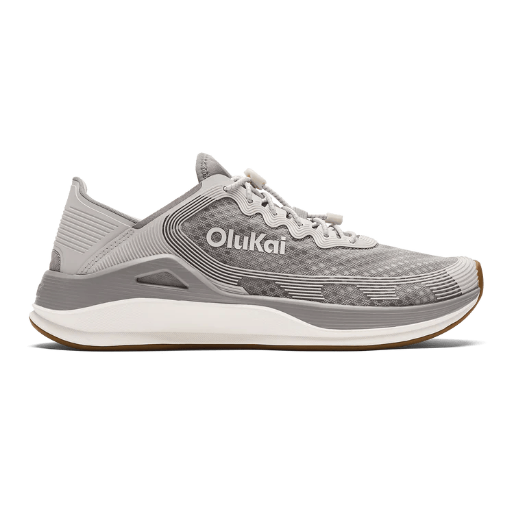 The OLUKAI Mens Ahi Ash/Sterling sneaker features a gray textured upper, white laces, and a white midsole, offering barefoot comfort. Shown from the side on a transparent background.