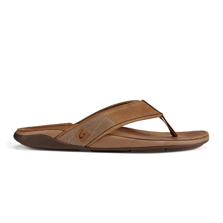 The OLUKAI Mens Tuahine Toffee flip-flop features a textured, Hawaiian-inspired strap, open toe design, cushioned footbed, and slightly raised sole in brown, shown from the side against a white background.