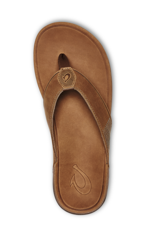 The OLUKAI Mens Tuahine Toffee is a brown leather flip-flop sandal with a fabric thong strap, waterproof leather, and a stitched logo near the top, shown from above on a plain background.