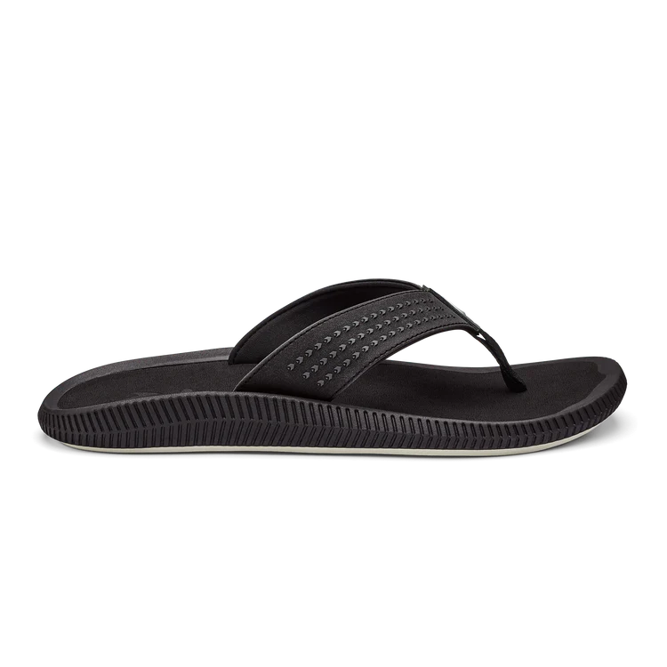The OLUKAI Mens Ulele Black sandal features water-resistant material, a textured sole, and a Wide perforated strap for foot comfort. Shown in side view on a white background.