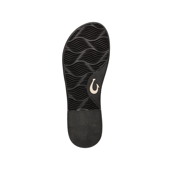 The OLUKAI Womens La‘i T–Bar Lava Rock features a black wavy-textured sole with a light-colored hook logo near the arch, seen from the bottom on a white background—perfect for those seeking comfortable T-Bar sandal style.