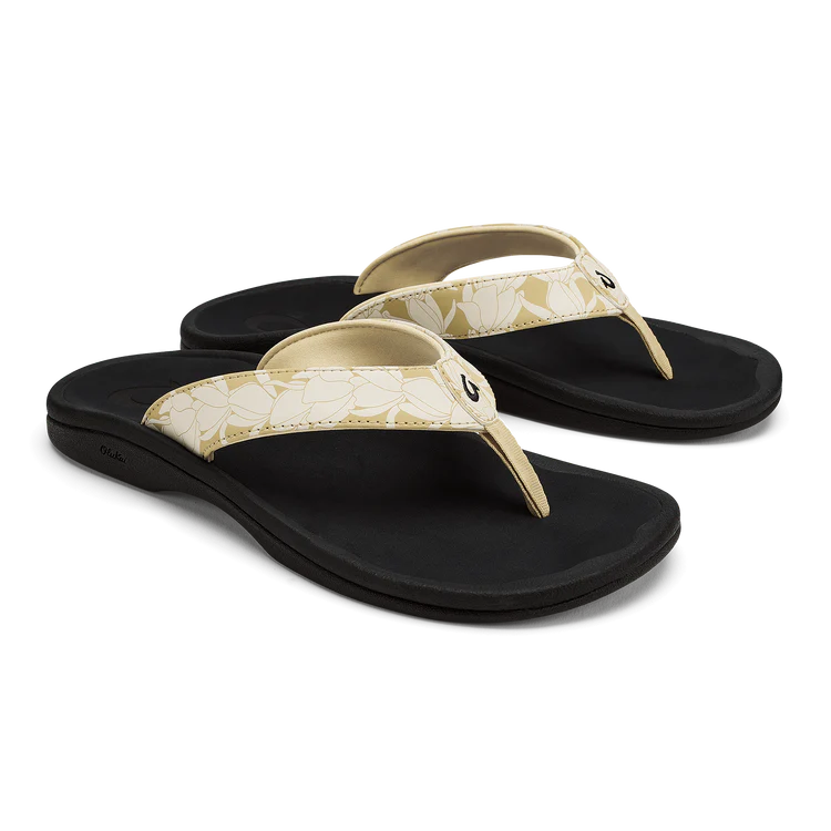 The OLUKAI Womens Ohana Toasted Coconut sandals feature cream-colored floral straps and black soles. These water-resistant flip-flops offer a comfortable, casual design with an anatomical footbed for all-day support.