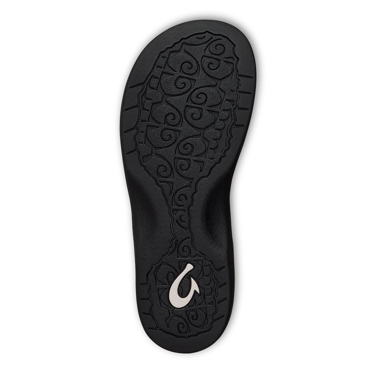 The Olukai Womens Ohana Toasted Coconut sandal features a black sole with a swirly texture, OLUKAI’s white wave-like logo near the heel, an anatomical footbed, and comes on a transparent background.