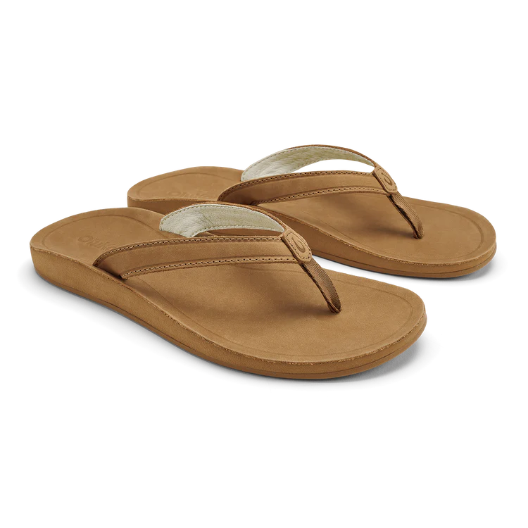 A pair of OLUKAI Womens Southshore Toffee flip-flop sandals featuring tan fabric straps, a cushioned sole, and a durable Wet Grip Rubber® outsole, shown against a plain white background.
