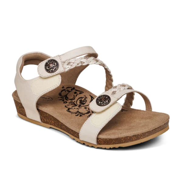 The Aetrex Womens Jillian Ivory by Aetrex features a beige open-toe design, low wedge heel, braided strap, adjustable closures with decorative buttons, floral cushioned insole, and an orthotic footbed for comfort.