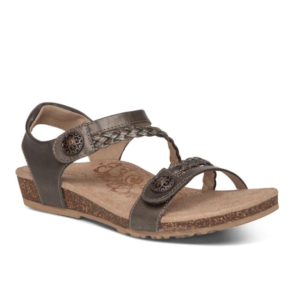 The Aetrex Womens Jillian Bronze sandal features brown open-toe design, braided and smooth straps with metal accents, a low wedge heel, cork-textured sole, and plush memory foam cushioning for all-day comfort.