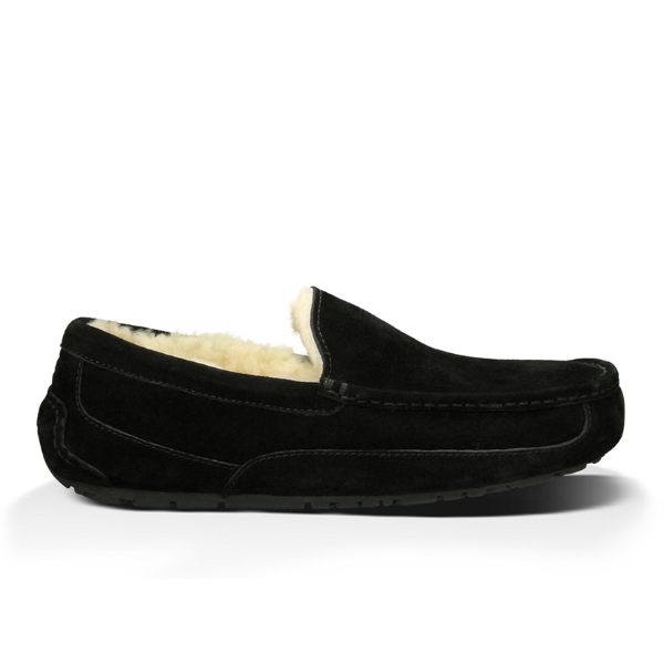 The UGG Mens Ascot Slipper Black by UGG features black suede, visible stitching, a soft cream fleece lining, and a flat rubber sole for long-lasting comfort. Shown in side profile against a white background.