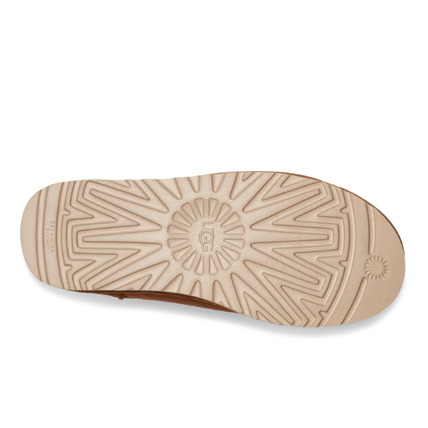 The image displays the bottom view of the UGG Mens Classic Slip-On Chestnut, featuring a tan sole with a geometric tread and the UGG logo embossed at the center—showcasing slip-on comfort and signature style.