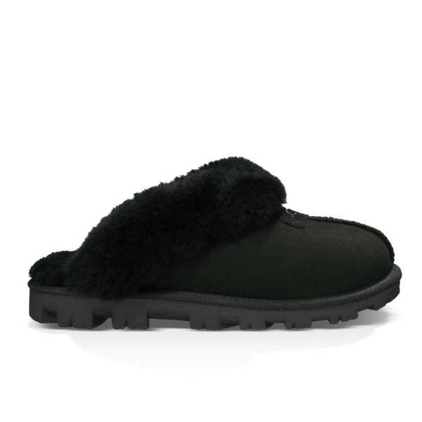 The UGG Womens Coquette Slipper Black features a thick textured sole and plush sheepskin lining, offering cozy comfort and foot support. The slipper is shown from the side against a white background.