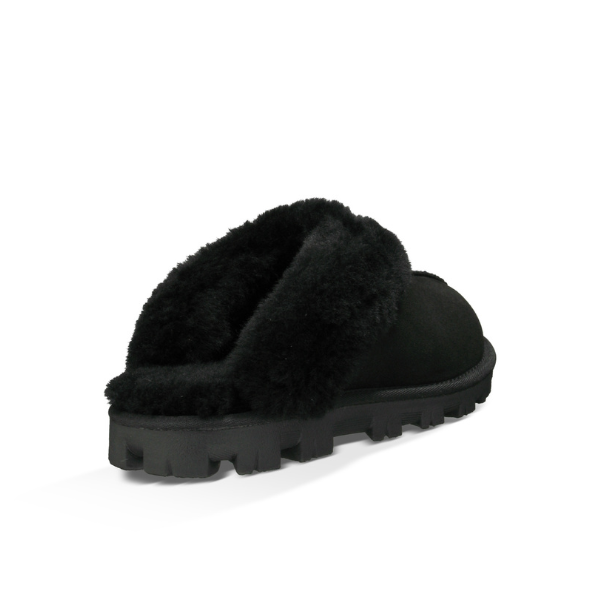 The UGG Womens Coquette Slipper in black is shown from a rear side angle on a white background, featuring thick, fluffy lining and a rugged sole for cozy comfort and foot pain relief.