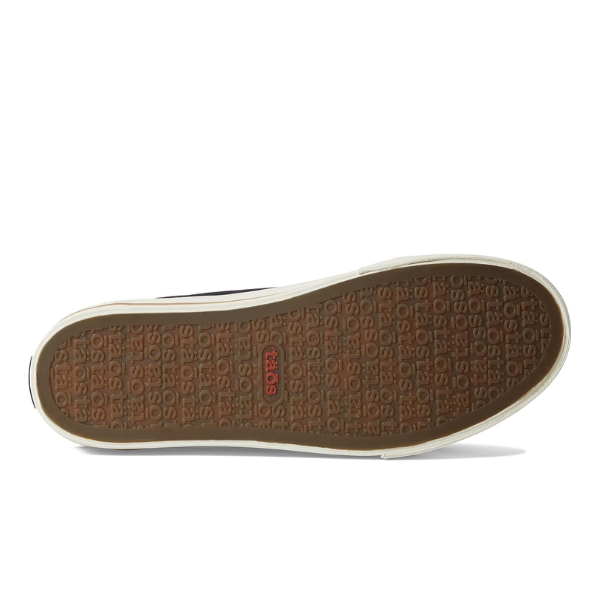 The image shows the sole of the Taos Womens Z Soul Black/Tan Distressed shoe by TAOS, featuring a brown rubber tread with repeated TAOS branding, a single red TAOS logo at the center, and contoured arch support for comfort.