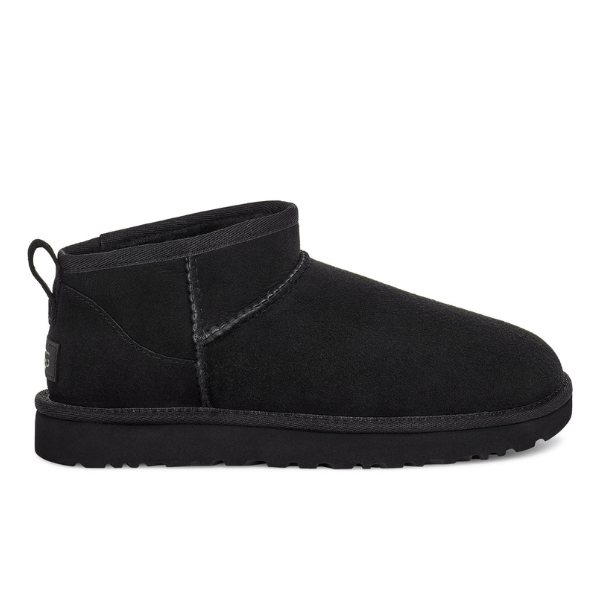 The UGG Womens Classic Ultra Mini Boot Black, an ankle-high suede boot with visible stitching, heel pull tab, and flat textured sole, is shown in side profile against a white background.