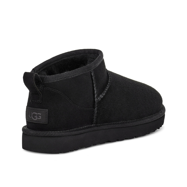 The UGG Womens Classic Ultra Mini Boot Black features soft sheepskin lining, visible stitching, a pull tab, black rubber sole, short ankle height, and a UGG logo heel label.