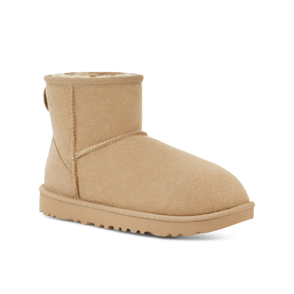 The UGG Womens Classic Mini II Boot in Mustard Seed is an ankle-height tan suede winter boot with a flat sole, visible stitching, soft fuzzy lining for comfort, and a textured rubber outsole, shown on a white background.