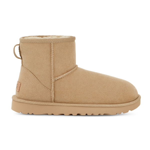 A tan suede UGG Womens Classic Mini II Boot in Mustard Seed, with a flat, ridged sole and plush cream lining for cozy foot comfort, shown in right-facing profile.