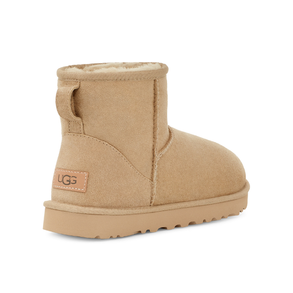 The UGG Womens Classic Mini II Boot in Mustard Seed features tan sheepskin, a shearling lining, thick sole, heel logo patch, and pull tab for easy wear. Designed by UGG for comfort and possible foot pain relief.