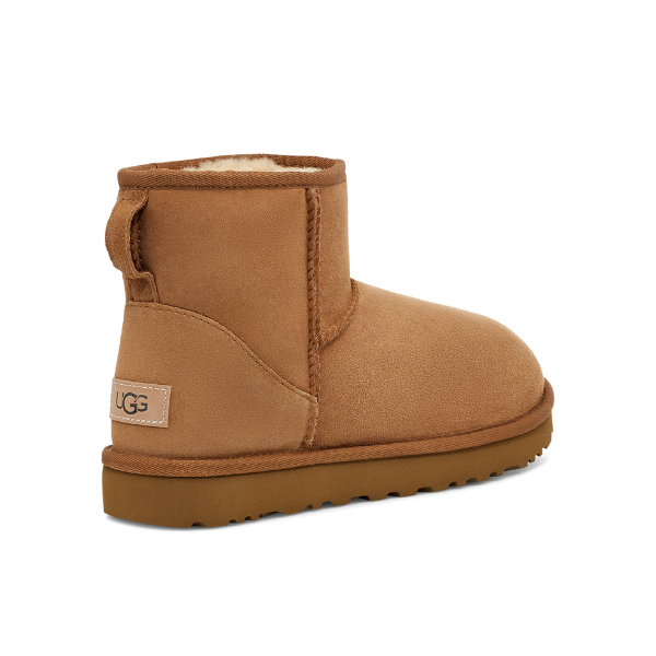 The UGG Womens Classic Mini II Boot Chestnut is a tan suede ankle boot with a pull tab, soft fleece lining, flat rubber sole, and stitched UGG logo label—perfect sheepskin boots for comfort and style.