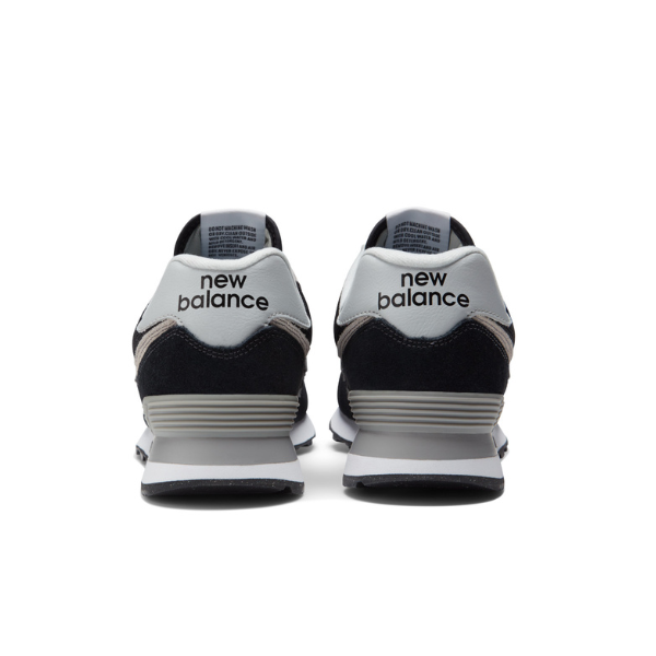 A pair of NEW BALANCE Men's 574 Black/White running shoes viewed from the back, featuring the brand's logo on a white-gray heel and black, gray, and white accents designed for foot pain relief.