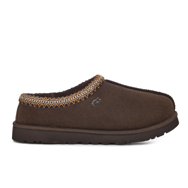 The UGG Mens Tasman Slippers Brown feature a brown suede slip-on upper, stitched patterned collar, side UGG logo, rounded toe, sheepskin lining, and a thick textured rubber sole.