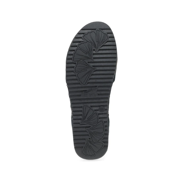 The image shows the black rubber sole of the Dansko Womens Mae Black Suede by DANSKO, featuring horizontal grooves and leaf-shaped patterns for traction and foot pain relief, set against a white background.