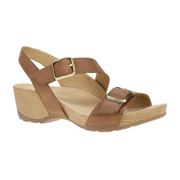 The Dansko Women’s Trinity Tan Burnished Nubuck sandal by DANSKO features two adjustable buckle straps, a low textured wedge heel, cushioned insole, arch support for foot pain relief, and an open toe and back for breathability.