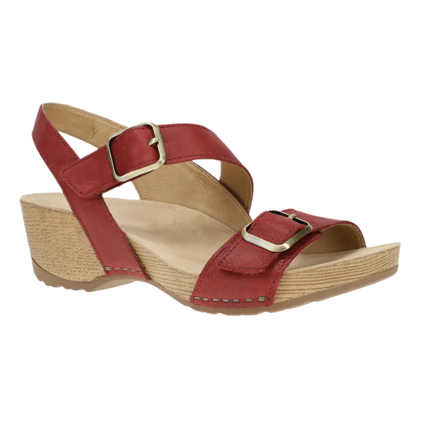 The Dansko Womens Trinity Cayenne Burnished sandal by DANSKO features a red design with a low wedge heel, tan sole, and two adjustable gold-buckle straps, offering stylish arch support and all-day comfort.